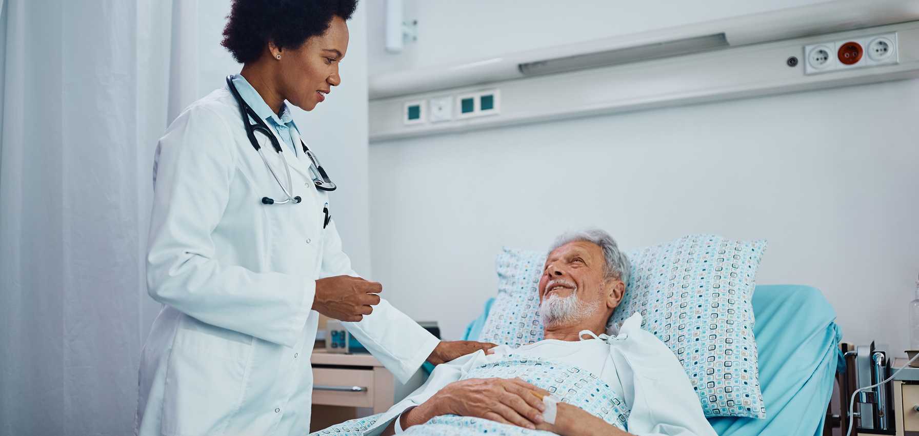 Doctor speaking with a smiling elderly male patient in a hospital bed